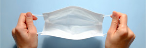 First person view of a woman holding face mask over blue textured table background. Protective raspiratory mask for spreading virus. Close up, copy space, top view, flat lay.