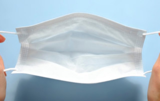 First person view of a woman holding face mask over blue textured table background. Protective raspiratory mask for spreading virus. Close up, copy space, top view, flat lay.